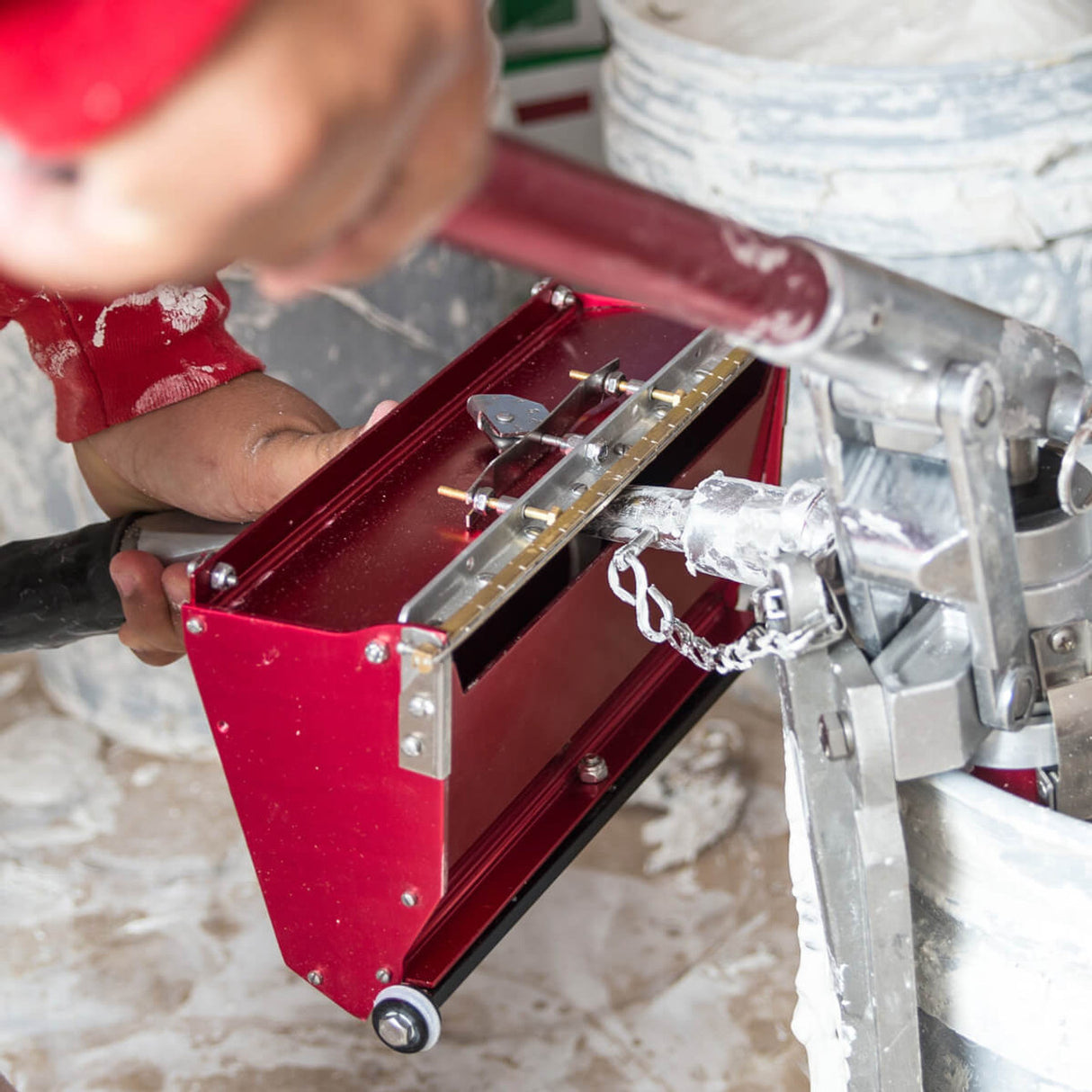 Person using Level 5 box filler attached to a compound pump to load mud from a bucket into a Level 5 flat box