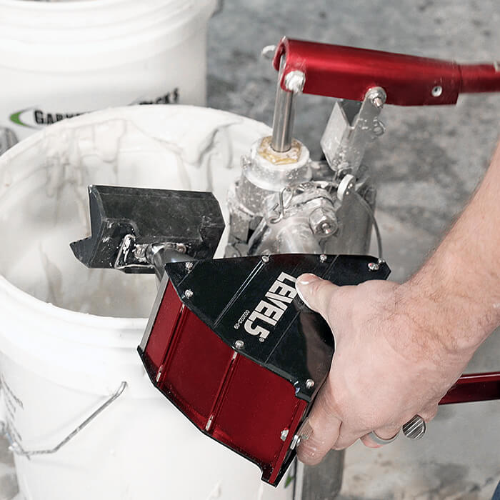 Person using Level 5 box filler attached to a compound pump to load mud from a bucket into a Level 5 nail spotter